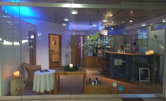 © Schönzeit | Sebastian Riezler An inviting reception area with a bright, modern design. On the table, there is a candle and there are various products on the counter. | © Schönzeit | Sebastian Riezler