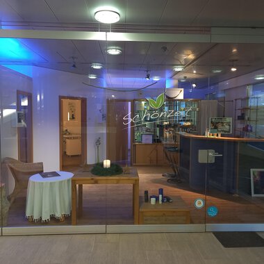 Ein einladender Empfangsbereich mit einem hellen, modernen Design. Auf dem Tisch steht eine Kerze und es gibt unterschiedliche Produkte auf der Theke. | © Schönzeit | Sebastian Riezler