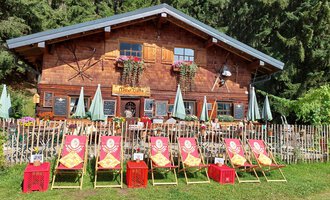 A traditional wooden house surrounded by trees. In front of the house are deck chairs and umbrellas in a friendly atmosphere. | © Maxhütte | Viera Krafcik