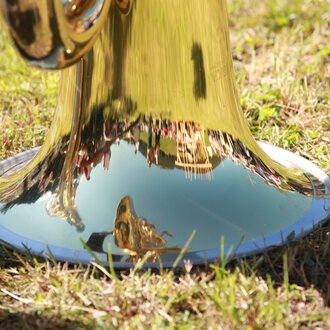 © Kleinwalsertal Tourismus | Frank Drechsel A shiny trumpet standing on the grass. Trees and people can be seen in the reflecting metal. | © Kleinwalsertal Tourismus | Frank Drechsel