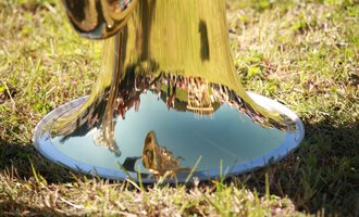 © Kleinwalsertal Tourismus | Frank Drechsel A shiny trumpet standing on the grass. Trees and people can be seen in the reflecting metal. | © Kleinwalsertal Tourismus | Frank Drechsel