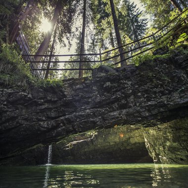 Ein idyllischer Ort mit klaren Gewässern und steilen Felsen. Im Hintergrund sind hohe Bäume und ein Sonnenstrahl sichtbar. | © Kleinwalsertal Tourismus | Oliver Farys