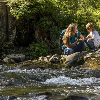 A mother and her son are sitting by a clear stream in nature. They are having fun and enjoying their time together. | © Kleinwalsertal Tourismus | Frank Drechsel