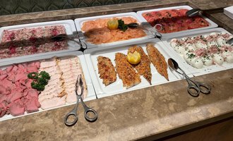 A table with a selection of various cold cuts, including ham, salmon, and cheese. The platters are beautifully arranged and decorated with fresh herbs. | © Almhof Rupp | Lukas Kind