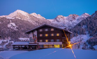 A cozy mountain house in the snow, surrounded by majestic mountains. The sky is tinted in soft shades of blue and violet. | © Hotel Alte Krone