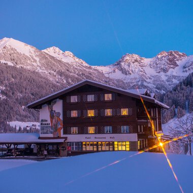 A cozy mountain house in the snow, surrounded by majestic mountains. The sky is tinted in soft shades of blue and violet. | © Hotel Alte Krone
