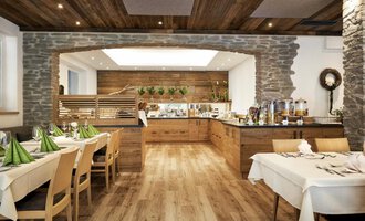 A cozy restaurant with wooden decor and an inviting buffet. The tables are elegantly set with green napkins. | © Robert Haller GmbH c/o Hotel Steinbock