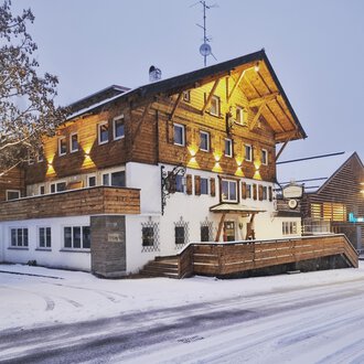 Ein charmantes Holzhaus im Schnee, beleuchtet von warmem Licht. Die Umgebung ist winterlich und einladend. | © Hotel Neue Krone GmbH | Werbewind GmbH