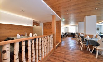 Ein modern gestaltetes Restaurant mit Holzwänden und einem einladenden Ambiente. Tische sind mit gedeckten Tellern vorbereitet, und der Boden ist aus Holz. | © Hotel Neue Krone GmbH | Werbewind GmbH