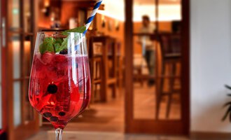 Ein erfrischendes Getränk in einem Glas mit einem blauen Strohhalm steht auf einem Tisch. Im Hintergrund ist eine gemütliche Bar zu sehen. | © Hotel Neue Krone GmbH | Werbewind GmbH