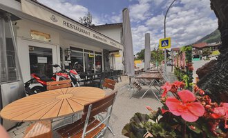 A restaurant with an inviting terrace and wooden tables.  
Blooming plants and a beautiful sky create a pleasant atmosphere. | © Riezlern Eck | Sead Sulejmani