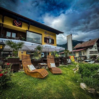 A cozy café with an inviting outdoor area. Two lounge chairs are situated on a green lawn, surrounded by plants and with a view of a charming building. | © Ristorante Monte Zaferna | K. Harmat-Hegedüs