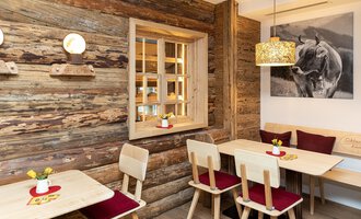 © Schönegger Käse-Alm Ein gemütliches Restaurant mit Holzvertäfelung und warmem Licht. Tische und Stühle laden zum Verweilen ein, während ein Kunstwerk an der Wand die Atmosphäre ergänzt. | © Schönegger Käse-Alm