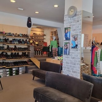 © Schuhhaus Schuster | Marietta Diehl Ein Schuhgeschäft mit zahlreichen Regalen voller Schuhe. In der Mitte stehen bequeme Sofas und Kleidung ist zur Schau gestellt. | © Schuhhaus Schuster | Marietta Diehl