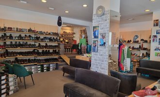 © Schuhhaus Schuster | Marietta Diehl Ein Schuhgeschäft mit zahlreichen Regalen voller Schuhe. In der Mitte stehen bequeme Sofas und Kleidung ist zur Schau gestellt. | © Schuhhaus Schuster | Marietta Diehl