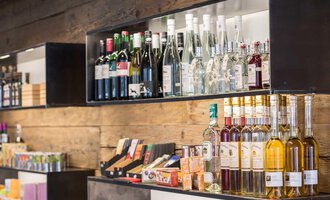 Shelves with various alcoholic beverages and snacks. The shelves are made of wood and display a selection of wines and spirits. | © Kleinwalsertal Tourismus | Frank Drechsel
