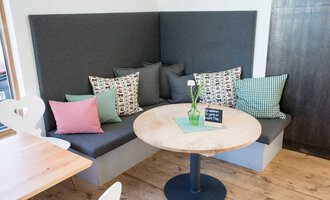 Eine gemütliche Sitzecke mit gepolsterten Kissen in verschiedenen Farben. Ein runder Holztisch steht in der Mitte, dekoriert mit einer kleinen Pflanze. | © Kleinwalsertal Tourismus | Frank Drechsel