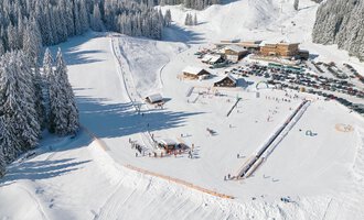 A snowy landscape with ski slopes and a restaurant nearby. Low clouds hang over the snow-covered trees. | © Skischule Hirschegg GmbH