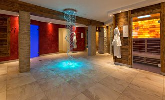 © Aparthotel Kleinwalsertal Haller GmbH & Co KG Ein moderner Wellnessbereich mit sanften Beleuchtungseffekten. An den Wänden befinden sich Holzelemente und Saunatüren. | © Aparthotel Kleinwalsertal Haller GmbH & Co KG