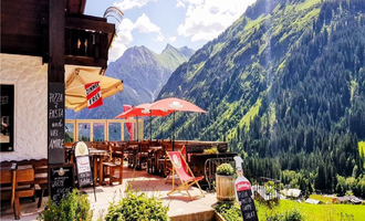 A cozy restaurant with terrace seating in the mountains. In the background, green forests and majestic mountains can be seen. | © Starzelhaus Pizzeria La Marmotta | J. Reich-Ulicny