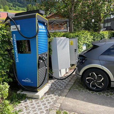 Eine Elektroladestation mit einem elektrischen Auto, das gerade aufgeladen wird. Die Umgebung ist grün und ruhig, umgeben von Bäumen. | © Energieversorgung Kleinwalsertal GmbH