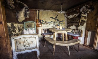 A rustic room with a round table and benches. Animal hides and decorative elements hang on the walls. | © Kleinwalsertal Tourismus | Oliver Farys