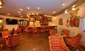 © IFA Hotel Alpenhof Wildental Eine gemütliche Bar mit einladenden Stühlen und einer warmen Beleuchtung. Im Hintergrund befindet sich eine gut gefüllte Bar und bunte Wandkunst. | © IFA Hotel Alpenhof Wildental