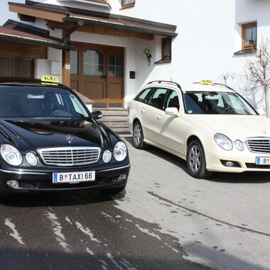 Two taxis are standing in front of a building. The black taxi is a limousine and the white taxi is an estate car. | © Taxi Beranek | Elmar Beranek