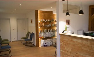 A modern reception area with wood paneling and elegant lamps. Exciting shelves display various products, and the seats are ready for visitors. | © Tierarztpraxis Oberstdorf | Regina Baumgartner