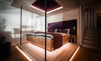 A modern bedroom with a wooden bed and elegant accents. Soft light creates a cozy atmosphere. | © Türtscher Die Schreinermanufaktur