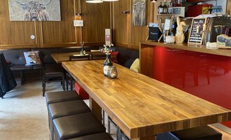A modern bar with a long wooden table and stylish high stools. The walls are in warm wood and red tones, creating a cozy atmosphere. | © Uusziit | Chantal Kessler
