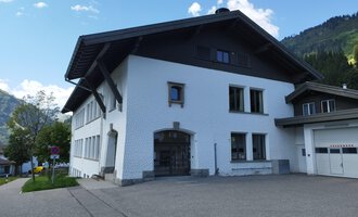 © Kleinwalsertal Tourismus | N. Lughammer Ein modernes, weißes Gebäude mit einem großen Dach. Es befindet sich in einer bergigen Umgebung mit grünem Gras und Bäumen. | © Kleinwalsertal Tourismus | N. Lughammer