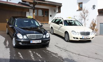 © Taxi Beranek | Elmar Beranek Zwei Taxis stehen vor einem Wohnhaus. Das schwarze Taxi und das weiße Kombi-Taxi sind bereit für Fahrgäste. | © Taxi Beranek | Elmar Beranek