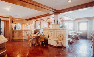 An inviting restaurant with wooden furniture and a warm ambiance. The bar area and tables are well arranged and offer a cozy atmosphere.