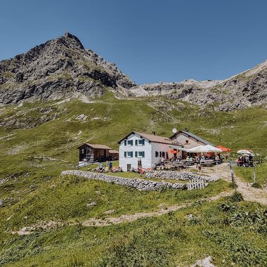 A picturesque mountain restaurant surrounded by green meadows and mountains. The clear sky provides a beautiful backdrop for the place. | © Widdersteinhütte  | Vanessa Wüstner