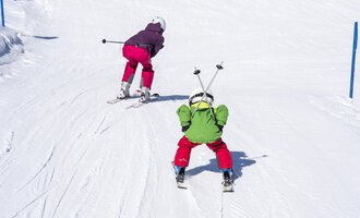 Two children are skiing on a snowy slope. They are wearing colorful ski outfits and enjoying the winter day. | © Kleinwalsertal Tourismus | Dominik Berchtold