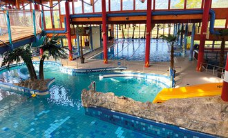 © WONNEMAR Ein farbenfrohes Hallenbad mit verschiedenen Becken und einer tropischen Atmosphäre. Palmen und Felsen schaffen ein entspannendes Ambiente. | © WONNEMAR