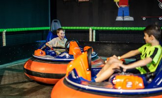 © Wonniland Sonthofen | interSPA Gruppe Zwei Kinder fahren mit elektronischen Bumper Cars in einer Sporthalle. Eines der Kinder hat einen Ausdruck voller Freude und Aufregung im Gesicht. | © Wonniland Sonthofen | interSPA Gruppe