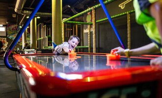 © Wonniland Sonthofen | interSPA Gruppe Ein Kind spielt begeistert an einem Air-Hockey-Tisch. Der Raum ist farbenfroh und einladend gestaltet. | © Wonniland Sonthofen | interSPA Gruppe