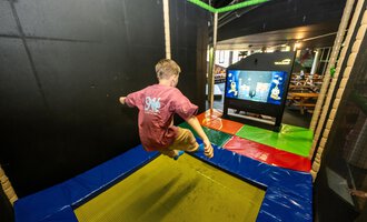 © Wonniland Sonthofen | interSPA Gruppe Ein Junge springt auf einem Trampolin in einem Spielbereich. Im Hintergrund ist ein Bildschirm mit Spielinhalten zu sehen. | © Wonniland Sonthofen | interSPA Gruppe