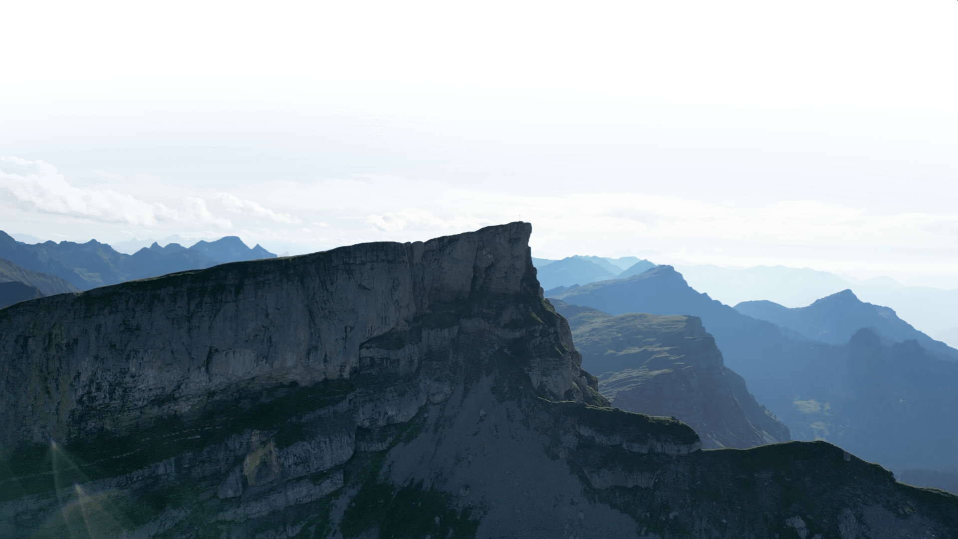 Eine dramatische Bergsilhouette mit einer markanten Kliffrand und geschichteten Gipfeln im Hintergrund unter einem bewölkten Himmel.